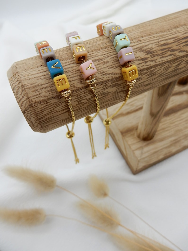 May include: Three adjustable bracelets with colorful beads that spell out the words "LOVE", "LIFE", and "JOY". Each bracelet has a gold chain and a sliding bead for adjusting the fit.