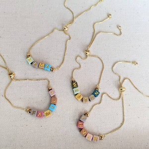 May include: Four gold chain bracelets with colorful letter beads spelling out the words "MAMA", "FAMILY", "WESTON", and "LOVER".