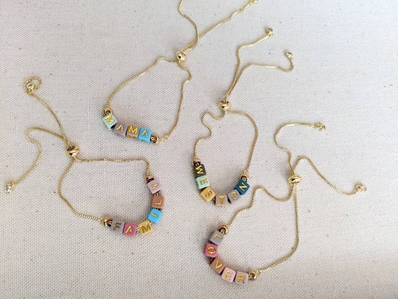 May include: Four gold chain bracelets with colorful letter beads spelling out the words "MAMA", "FAMILY", "WESTON", and "LOVER".