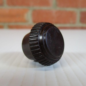 Può includere: Un pomello marrone scuro, in stile vintage, con un bordo scanalato e una parte superiore liscia e arrotondata. Il pomello è probabilmente in legno ed è progettato per mobili o uso decorativo.