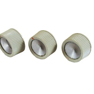 Può includere: Tre manopole di controllo cilindriche con un esterno a coste color bianco sporco e un centro circolare piatto color argento. Ogni manopola presenta una piccola e sottile linea indicatrice arancione sul bordo superiore del lato a coste.