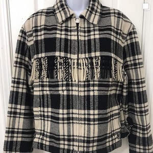 May include: A black and cream plaid jacket with a full zipper closure. The jacket features cream-colored fringe across the chest. The jacket has a collared neckline and is made of a woven fabric.