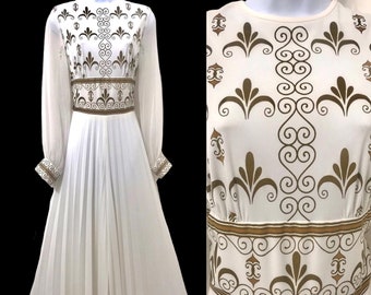 May include: A white maxi dress with long sleeves and a gold patterned design. The dress has a pleated skirt and a fitted bodice.