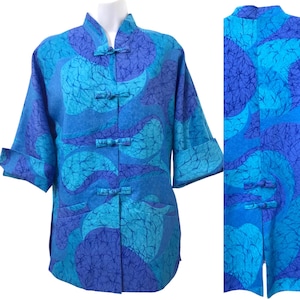 Puede incluir: Una camisa con estampado azul y morado con cuello mandarín y cierres de rana. La camisa tiene un corte holgado y mangas tres cuartos.