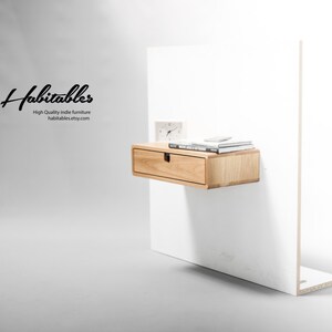 May include: A light wood floating shelf with a single drawer and a small clock and books on top. The shelf is mounted on a white wall. The text "Habitables High Quality indie furniture habitables.etsy.com" is visible in the image.