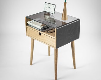 Puede incluir: Una mesita de noche de madera oscura con una tapa de vidrio y un cajón. La mesita de noche tiene una sola tulipa roja en un jarrón de madera y un pequeño reloj en la parte superior.