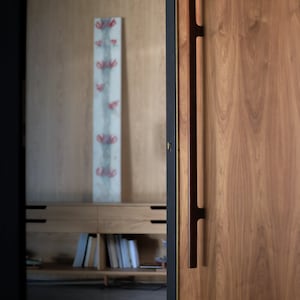 May include: A wooden door with a long, dark brown handle. The door is closed and has a black frame. The door is made of wood with a natural grain pattern.