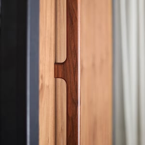 May include: A close-up of a dark brown wooden door handle. The handle is rectangular and has a simple design.