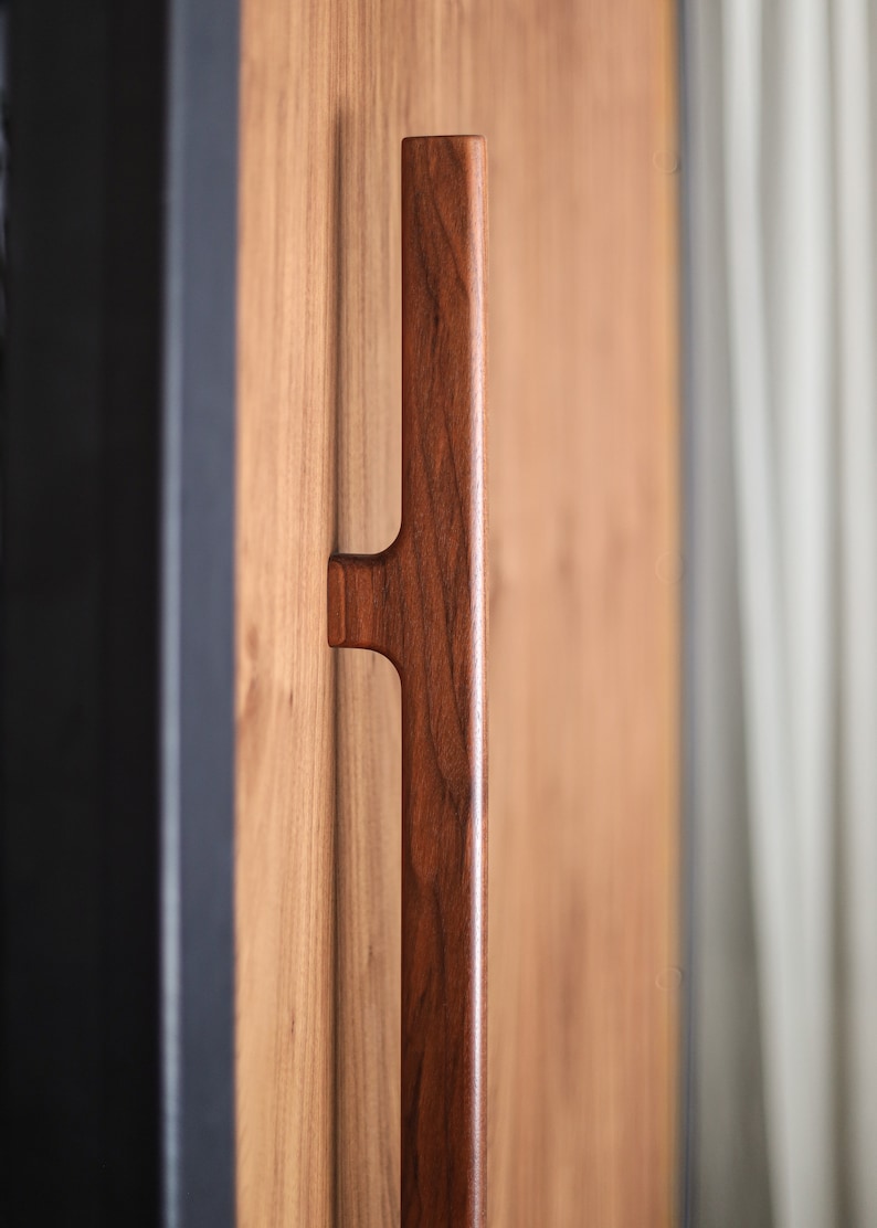 May include: A close-up of a dark brown wooden door handle. The handle is rectangular and has a simple design.