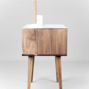 May include: A white and walnut wood nightstand with a white globe lamp on top. The nightstand has four legs and a drawer.