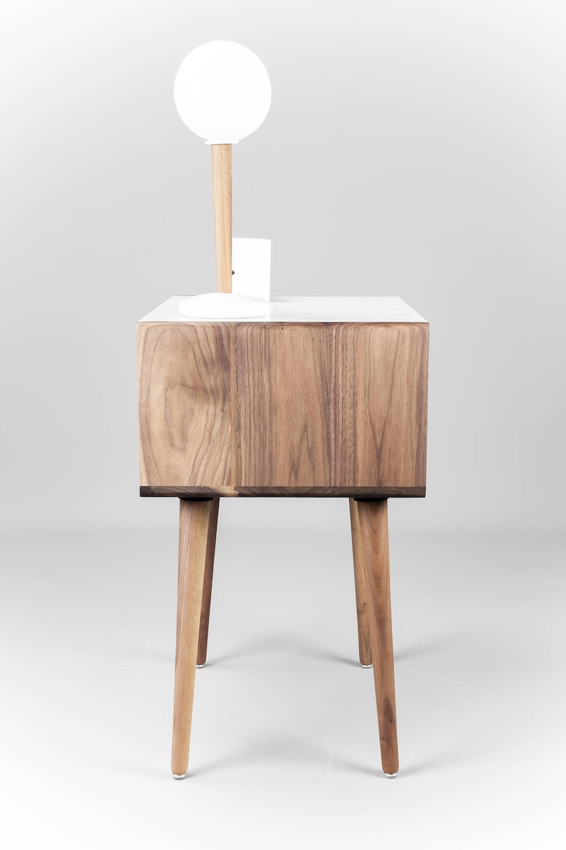 May include: A white and walnut wood nightstand with a white globe lamp on top. The nightstand has four legs and a drawer.