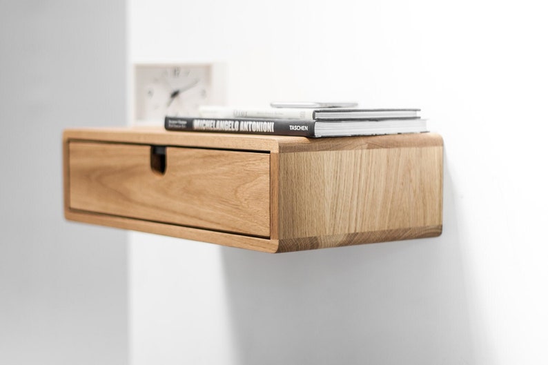 May include: A light wood floating shelf with a drawer and a stack of books on top. The books are titled "Michelangelo Antonioni" and "Taschen".