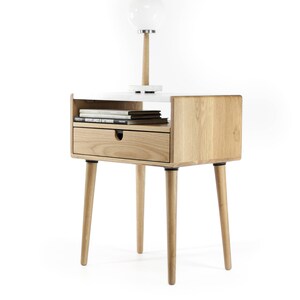 May include: A wooden end table with a white top and a drawer. The table has four legs and a shelf for books. A white globe lamp sits on the top of the table.