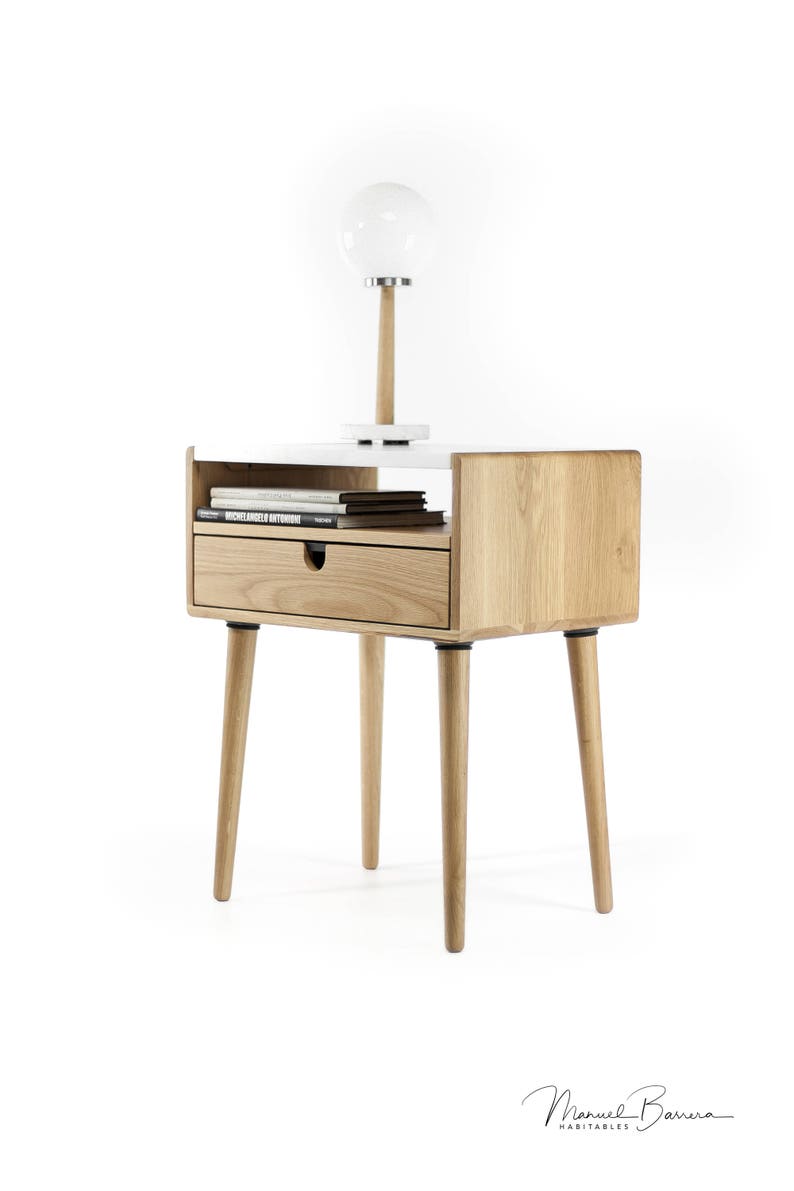 May include: A wooden end table with a white top and a drawer. The table has four legs and a shelf for books. A white globe lamp sits on the top of the table.
