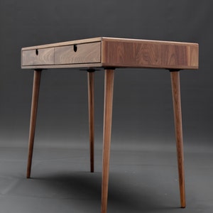 May include: A wooden desk with two drawers and four legs. The desk is made of walnut wood and has a natural finish.