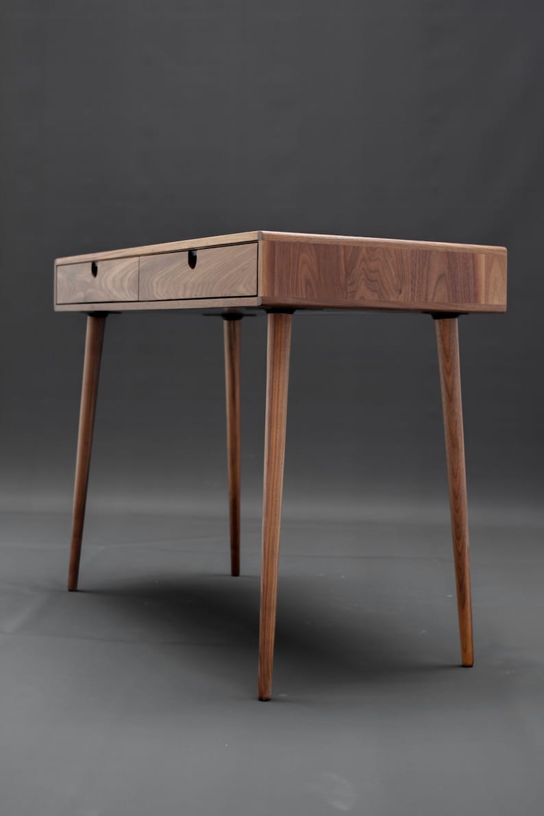 May include: A wooden desk with two drawers and four legs. The desk is made of walnut wood and has a natural finish.