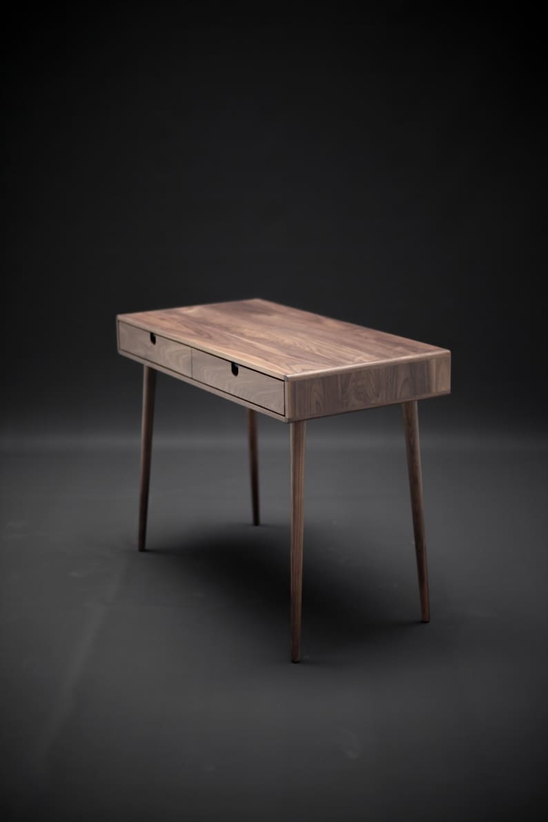 May include: A dark brown wooden desk with two drawers and tapered legs. The desk is on a black background.
