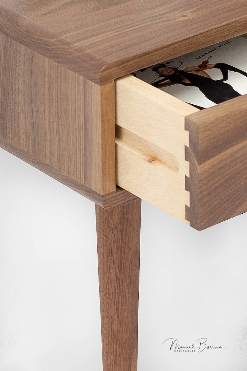 May include: A wooden end table with a drawer that is open, revealing a magazine inside. The table has a walnut finish and four legs.