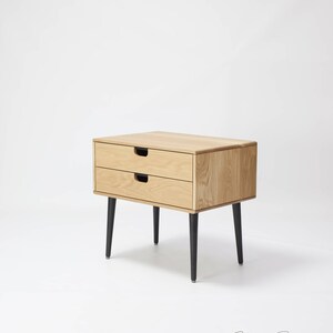 May include: A wooden nightstand with two drawers and black legs. The nightstand is made of light wood and has a simple, modern design.