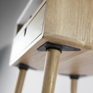 May include: A wooden side table with a drawer and four legs. The legs are made of wood and have black metal brackets at the bottom. The table is made of light wood and has a natural finish.