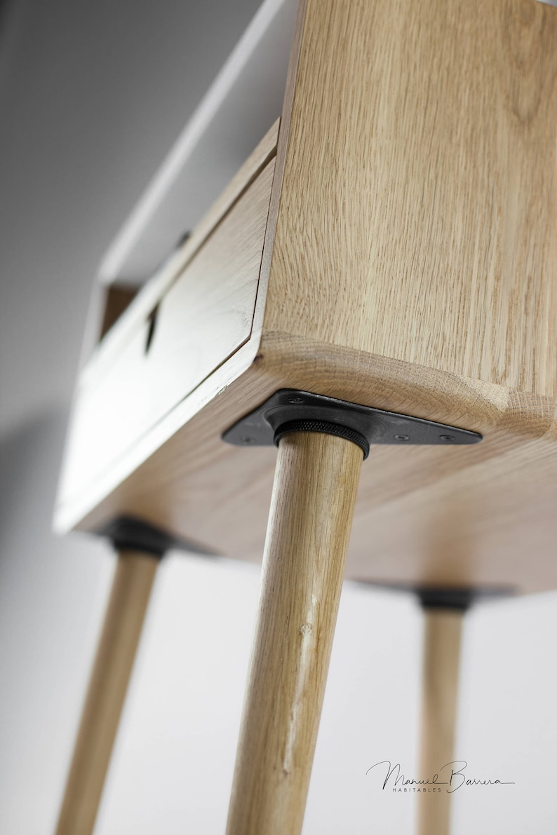 May include: A wooden side table with a drawer and four legs. The legs are made of wood and have black metal brackets at the bottom. The table is made of light wood and has a natural finish.