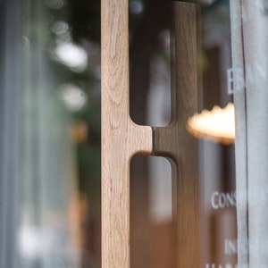 May include: A close-up of a wooden door handle with a unique design. The handle is made of light brown wood and has a simple, modern style.