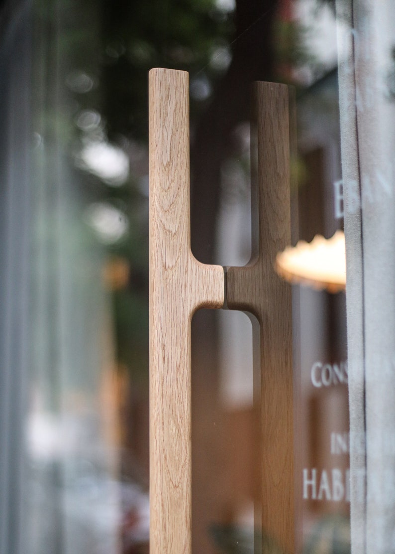 May include: A close-up of a wooden door handle with a unique design. The handle is made of light brown wood and has a simple, modern style.