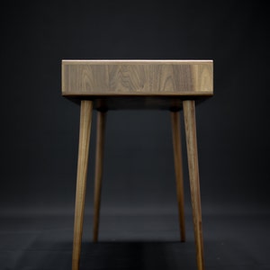May include: A wooden desk with a dark brown finish and four legs. The desk has a simple, modern design.