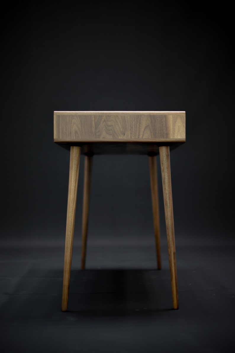 May include: A wooden desk with a dark brown finish and four legs. The desk has a simple, modern design.