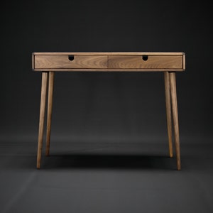 May include: A wooden desk with two drawers and tapered legs. The desk is made of dark wood and has a natural finish.