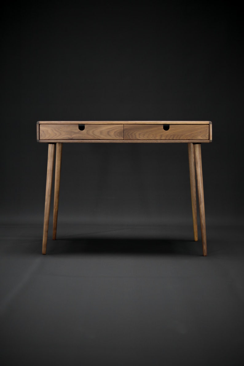 May include: A wooden desk with two drawers and tapered legs. The desk is made of dark wood and has a natural finish.