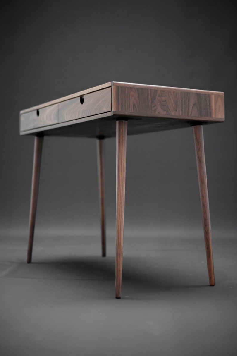 May include: A dark brown wooden desk with two drawers and tapered legs. The desk is made of solid wood and has a natural finish.