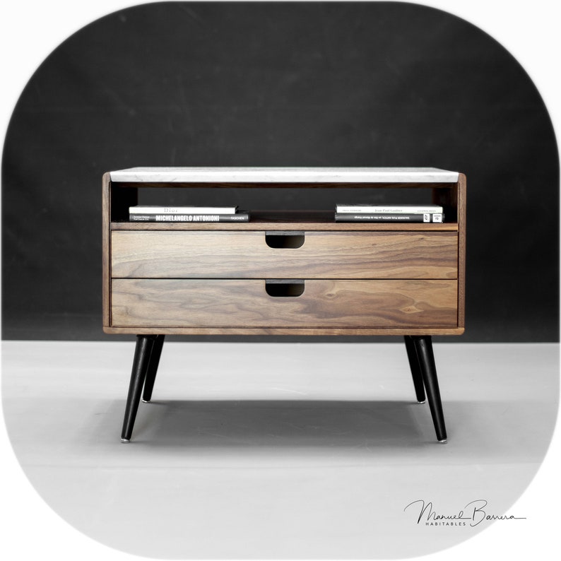 May include: A two-drawer wooden side table with a white marble top. The table has black legs and a shelf for storage. The drawers have black pulls. The table is in front of a black background.