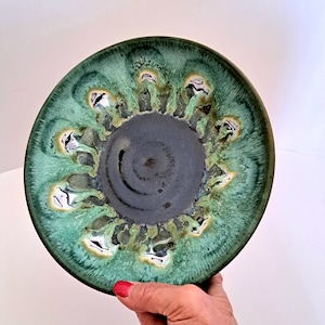 May include: A green ceramic bowl with a dark gray center and a swirling pattern. The bowl has a unique, hand-crafted look.
