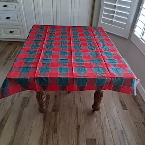May include: Red and green plaid tablecloth with a Christmas tree design. The tablecloth is on a wooden table with four legs.