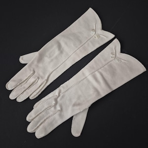 May include: A pair of off-white gloves featuring a scalloped wrist edge and delicate white embroidery detail near the opening. The gloves have visible stitching along the fingers and a smooth, matte finish, extending to the mid-forearm length.