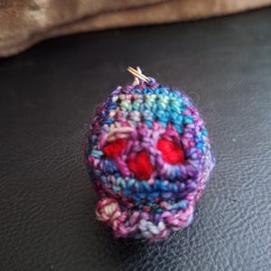 May include: A small, crocheted, multi-colored, round ornament with a red center and a gold loop at the top.