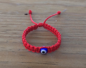 May include: Red string bracelet with a blue evil eye charm. The bracelet is tied with a knot and has a tassel on each end.