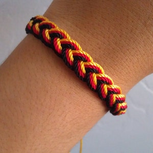 May include: A black, red, and yellow braided friendship bracelet with a yellow string hanging from the end.