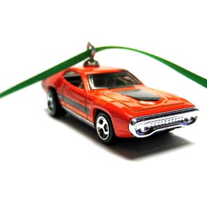 May include: A die-cast, orange classic car ornament with black racing stripes and a black hood. The car has chrome detailing on the front and wheels. A green ribbon is attached for hanging.