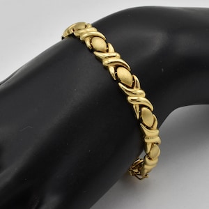 May include: A gold-toned bracelet with an alternating X and oval link design. The bracelet is displayed on a black surface. The links have a matte finish, and the X links have a polished finish.