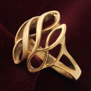 May include: A gold ring featuring an openwork design with multiple interlocking, curved metal loops that create a cage-like structure. The band is solid and tapers toward the back, while the front displays a series of interconnected, polished gold shapes.