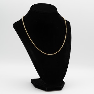 May include: A gold-colored rope chain necklace displayed on a black velvet bust. The necklace is thin and delicate, with a twisted rope design. The bust is set against a white background.