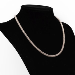 May include: A silver-toned chain necklace featuring a dense, woven wheat or foxtail link pattern. The metallic chain has a rounded, tubular profile and a consistent, uniform texture throughout its entire length, displaying a polished finish.
