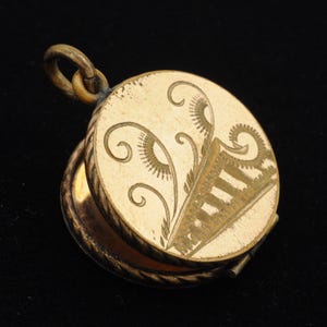 May include: A vintage gold-toned locket, open to reveal the interior. The locket features an ornate design on the front, with a decorative pattern. The locket is round and has a loop for a chain. The background is black.