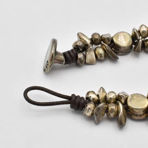 K&ouml;nnte beinhalten: Nahaufnahme eines silberfarbenen Armbands mit Lederband. Das Armband hat verschiedene Formen von Silberperlen und einen Verschluss mit der eingravierten Zahl "50". Das Lederband ist dunkelbraun.