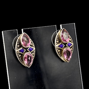 May include: A pair of silver stud earrings with pink teardrop-shaped gemstones and blue diamond-shaped accents. The earrings have a detailed, ornate design with small, round embellishments around the edges.