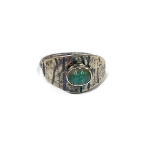 Op de afbeelding: Een zilveren ring met een getextureerde band en een groene ovale edelsteen. De band van de ring heeft een ruwe, schorsachtige textuur en de edelsteen is gezet in een eenvoudige bezel.