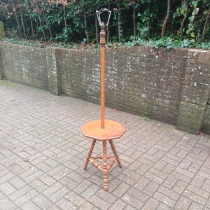 May include: A vintage wooden coat stand with a hexagonal table base and a tall, slender pole. The stand features a decorative metal top and stands on a three-legged base. The wood has a warm, natural finish.