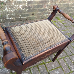 May include: An antique wooden chair with a patterned fabric seat. The chair has turned wooden armrests and legs. The dark brown wood has a rich finish, and the seat is a neutral beige colour. The chair is designed with a unique, curved shape.